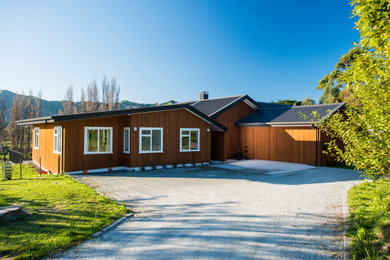 Diseño de fachada de casa marrón moderna de tamaño medio de una planta con revestimiento de madera, tejado a dos aguas y tejado de metal