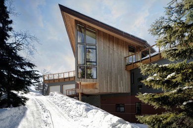 Esempio della villa marrone contemporanea a due piani di medie dimensioni con rivestimento in legno e tetto a padiglione