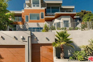 Example of a large minimalist gray three-story stucco exterior home design in Los Angeles with a metal roof