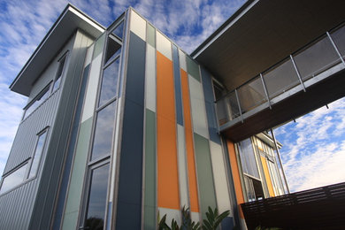 Cette image montre une façade de maison métallique et grise marine à un étage avec un toit plat.