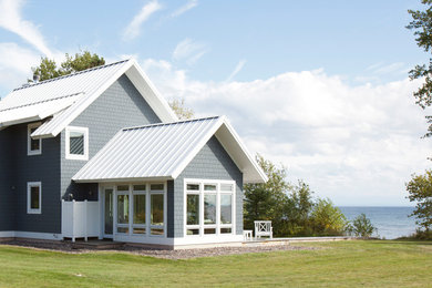 Modelo de fachada de casa gris costera pequeña de dos plantas con revestimiento de aglomerado de cemento, tejado a dos aguas y tejado de metal