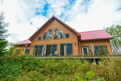Modelo de fachada de casa multicolor rural grande de dos plantas con revestimiento de madera, tejado a dos aguas y tejado de metal