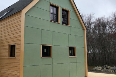 Cette image montre une façade de maison verte design en panneau de béton fibré à un étage avec un toit à deux pans et un toit en shingle.