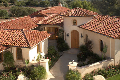 Diseño de fachada de casa beige mediterránea de tamaño medio de dos plantas con revestimiento de estuco, tejado a cuatro aguas y tejado de teja de barro