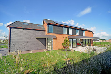 Modelo de fachada roja actual de tamaño medio de dos plantas con revestimiento de ladrillo y tejado a dos aguas