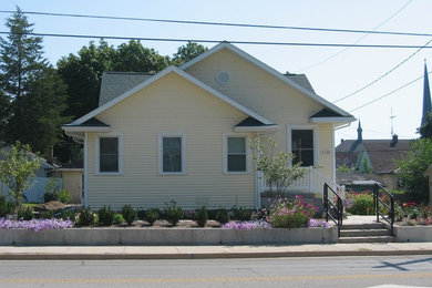 Diseño de fachada de casa amarilla de estilo americano de tamaño medio de una planta con revestimiento de madera, tejado a dos aguas y tejado de teja de madera
