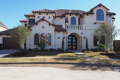 Large tuscan beige two-story stucco exterior home photo in Dallas with a hip roof