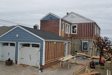 Imagen de fachada de casa azul marinera de tamaño medio de dos plantas con revestimiento de vinilo, tejado a cuatro aguas y tejado de teja de madera