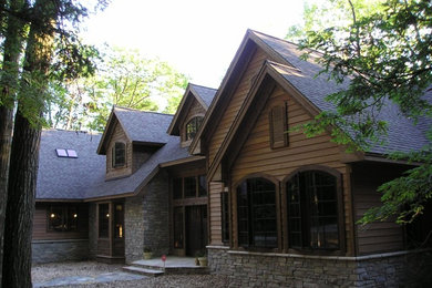 Large and brown rustic bungalow detached house in Other with stone cladding, a hip roof and a shingle roof.