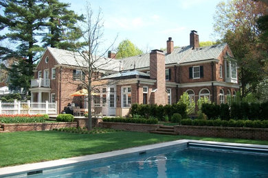 Large and red classic two floor brick detached house in New York with a pitched roof and a shingle roof.