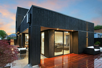 Modelo de fachada de casa pareada negra contemporánea grande de dos plantas con revestimiento de madera, tejado plano y tejado de metal