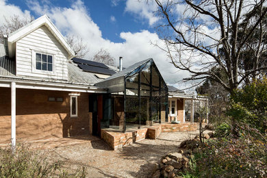 Foto de fachada de casa marrón actual pequeña de dos plantas con revestimiento de vidrio, tejado a dos aguas y tejado de metal