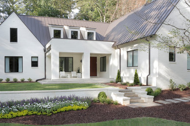 Esempio della facciata di una casa grande bianca classica a due piani con rivestimento in mattoni, tetto a capanna e copertura in metallo o lamiera