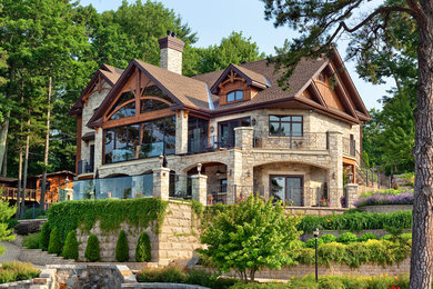Ejemplo de fachada de casa beige de estilo americano extra grande de tres plantas con revestimiento de piedra, tejado a dos aguas y tejado de teja de madera