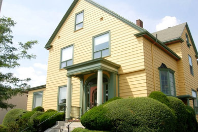 Ejemplo de fachada de casa amarilla clásica de tamaño medio de dos plantas con revestimiento de madera, tejado a cuatro aguas y tejado de teja de madera