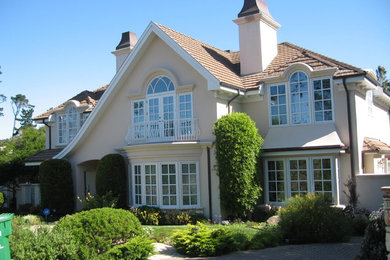 Inspiration pour une façade de maison beige traditionnelle en stuc à un étage et de taille moyenne avec un toit à quatre pans et un toit en tuile.