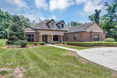 Large elegant red one-story brick and board and batten exterior home photo in Orlando with a shingle roof and a gray roof