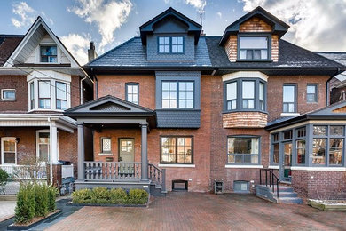 Example of a large classic red three-story brick exterior home design in Toronto with a hip roof