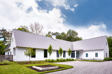 Imagen de fachada de casa blanca campestre grande de una planta con revestimiento de madera, tejado a dos aguas y tejado de metal