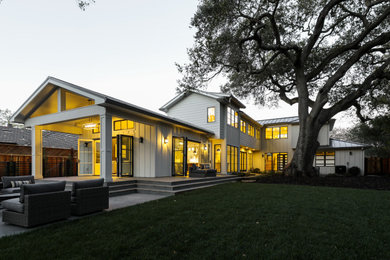 Esempio della villa bianca country a due piani con rivestimento in legno, tetto a capanna e copertura in metallo o lamiera
