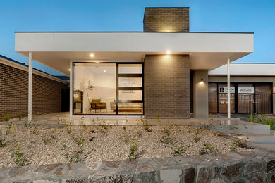 На фото: кирпичный, серый дом среднего размера в стиле ретро с разными уровнями и вальмовой крышей