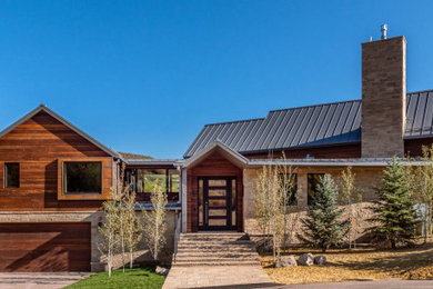 Imagen de fachada de casa marrón y gris rural con revestimientos combinados, tejado a dos aguas y tejado de metal