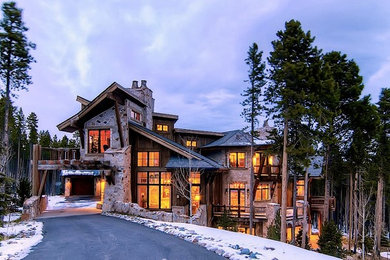 Large mountain style brown three-story stone house exterior photo in Denver with a hip roof and a tile roof