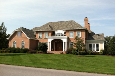 Inspiration for a large timeless red two-story brick house exterior remodel in Other with a hip roof and a shingle roof