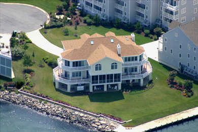 Example of a large beach style beige three-story stucco house exterior design in Other with a hip roof and a shingle roof