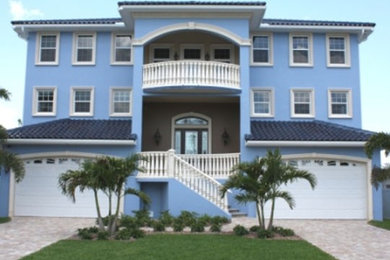 Large tropical blue three-story stucco exterior home idea in Tampa with a hip roof