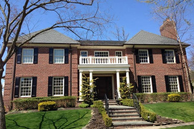 Example of a large classic red two-story brick house exterior design in New York with a hip roof and a shingle roof