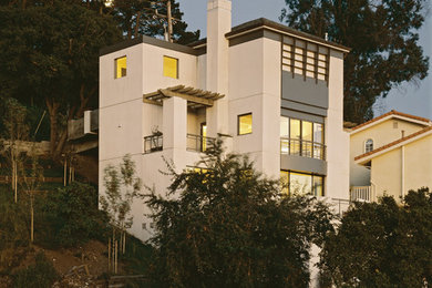 Cette image montre une petite façade de maison blanche design en stuc à deux étages et plus avec un toit à quatre pans et un toit en tuile.