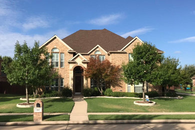 Large elegant red two-story brick house exterior photo in Dallas with a hip roof and a shingle roof