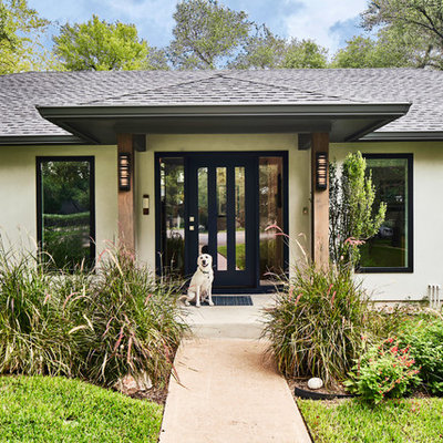 Example of a large 1960s gray one-story stucco house exterior design in Austin with a hip roof and a shingle roof