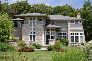 Imagen de fachada de casa gris actual grande de dos plantas con revestimientos combinados y tejado a cuatro aguas