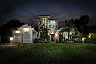 Imagen de fachada blanca tropical grande de dos plantas con revestimiento de estuco y tejado a dos aguas