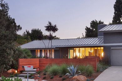 Small and gey modern two floor render detached house in Santa Barbara with a pitched roof and a metal roof.