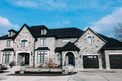 Huge transitional gray two-story stone house exterior idea in Toronto with a hip roof and a shingle roof