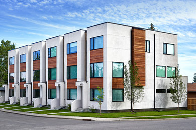 Example of a mid-sized minimalist white three-story stucco flat roof design in Calgary