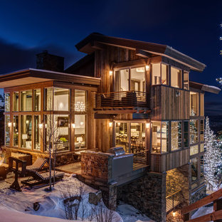 Foto della facciata di una casa unifamiliare grande marrone rustica a tre piani con rivestimento in legno, tetto a capanna e copertura in metallo o lamiera