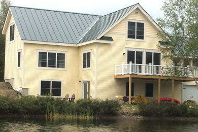 Modelo de fachada de casa amarilla campestre de tamaño medio de dos plantas con revestimiento de aglomerado de cemento, tejado a dos aguas y tejado de metal
