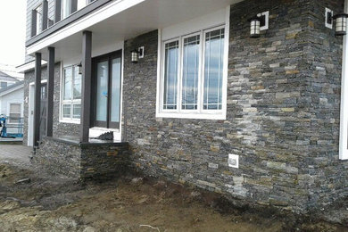 This is an example of a medium sized and gey traditional two floor house exterior in Boston with stone cladding.