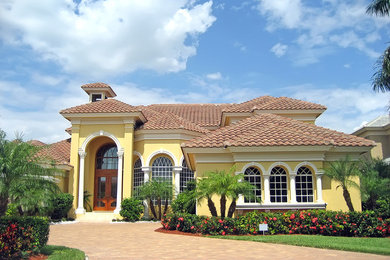 Foto de fachada de casa amarilla clásica grande de dos plantas con revestimiento de estuco, tejado a cuatro aguas y tejado de teja de barro