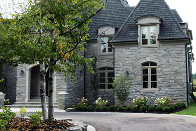 Large and beige classic detached house in Toronto with three floors, stone cladding, a mansard roof and a shingle roof.