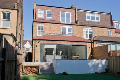 Photo of a medium sized and red contemporary brick detached house in London with three floors, a hip roof and a tiled roof.