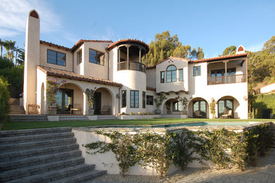 Large and beige mediterranean two floor render house exterior in Los Angeles with a pitched roof.