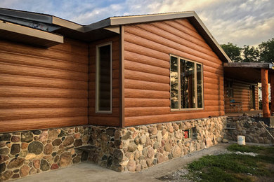 Foto della villa grande marrone rustica a un piano con rivestimento in legno e tetto a capanna