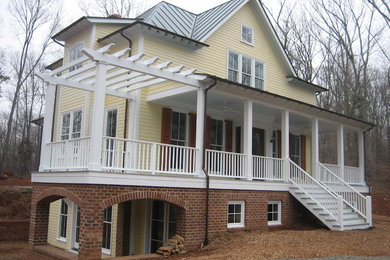 Mid-sized elegant yellow three-story vinyl house exterior photo in Other with a hip roof and a metal roof