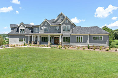 Example of a large arts and crafts gray two-story vinyl house exterior design in Other with a clipped gable roof and a shingle roof