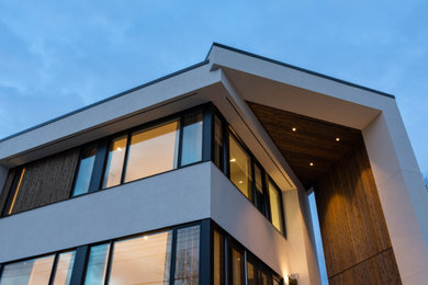 This is an example of a white midcentury detached house in Calgary with three floors, mixed cladding and a flat roof.